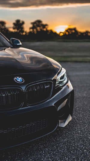 黑色BMW M汽車在日落時停泊在瀝青路上，背景有樹木。