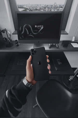 手拿黑色iPhone，面前是現代科技辦公桌，可欣賞城市景觀。 — 黑色動態圖 壁紙