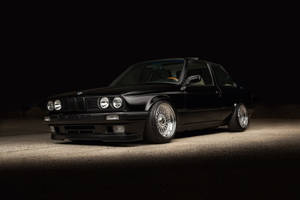 黑色BMW E30雙門轎跑車配備定制輪圈，在夜間沙漠環境中照亮。