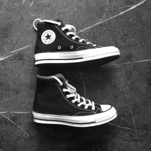 黑色Converse運動鞋，白色鞋帶，放在有刮痕的灰色混凝土地板上。