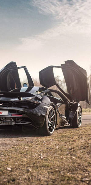 黑色McLaren跑車，鷗翼門打開，日落時停在草地上。 — 草 壁紙