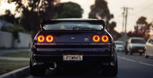 黑色日產Skyline GT-R，帶有發光的橙色尾燈，停在日落時分的街道上。 — 汽車 壁紙