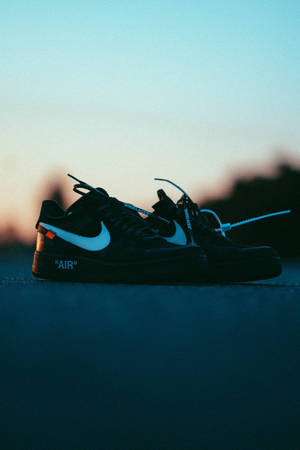 黑色Nike Air Force 1運動鞋，帶有白色swoosh和橙色標籤，在日落時分的路面上。
