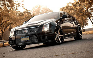 黑色Cadillac CTS-V停在路上，背景是金色夕陽和樹木。