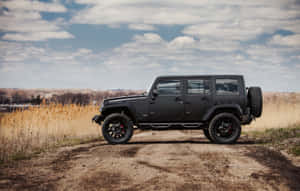 日落時分，黑色Jeep Wrangler停在草地上的泥路