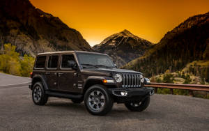 日落時分黑色Jeep Wrangler在山路上，背後是積雪的山峰。