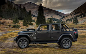 黑色Jeep Wrangler停在山徑上，周圍環繞著樹木和山丘。