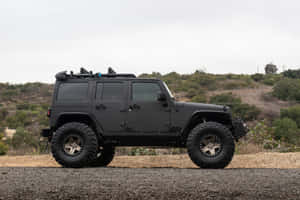 啞光黑色升高Jeep Wrangler停泊在碎石上，背景有灌木山丘。
