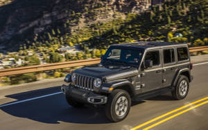 黑色Jeep Wrangler在山路上行駛，背景有森林和峭壁
