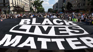 抗議者在日間示威期間，帶著一面大型 Black Lives Matter 橫幅穿過城市街道。 — 黑白 壁紙