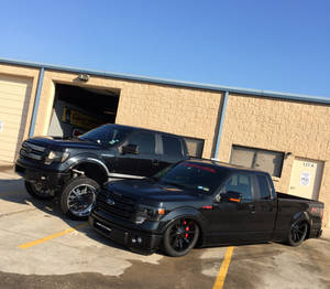 兩輛黑色訂製福特F-150皮卡車停放在車庫前。