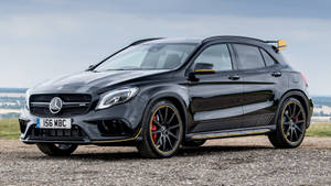 黑色 Mercedes-AMG GLA45 S SUV，帶黃色飾條和紅色制動器，停在礫石場上。