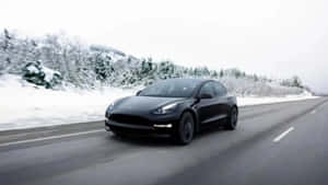 黑色Tesla Model Y在冬季森林中的雪路上行駛。