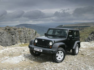 黑色Jeep Wrangler在岩石懸崖上俯瞰陰天下的山脈