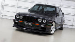 黑色BMW M3跑車帶橙色飾邊停在白色車庫中。