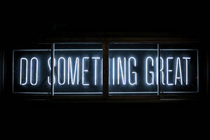 一個明亮的白色霓虹燈牌，上面寫著「Do Something Great」，在黑暗的窗戶中。