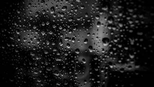 玻璃上的雨滴遮擋了模糊的灰階城市景觀。
