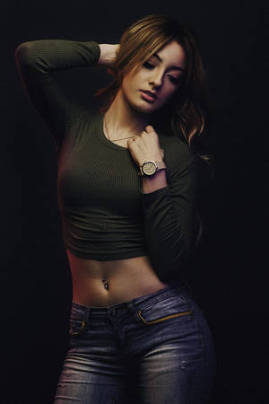 一位身穿綠色短版上衣和牛仔褲的女性將一隻手放在頭髮上擺姿勢。