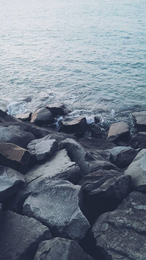 海浪在海洋岸邊的深灰色岩石上破碎。 — iPhone 7 Plus 壁紙