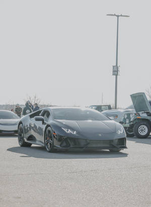 啞光黑色林寶堅尼 Huracán 停泊在陽光明媚的停車場，附近有人群。