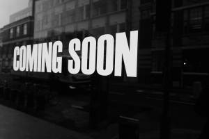 玻璃店面帶有街道倒影的「COMING SOON」標誌黑白照片。