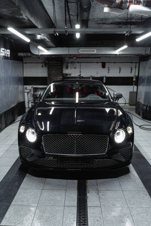 光線充足的工業車庫中，瓷磚地板上的黑色賓利 Continental GT。