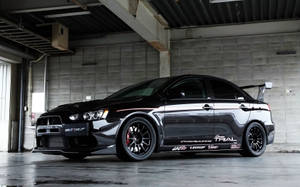 黑色三菱Lancer Evolution拉力賽車在混凝土車庫內，帶有贊助商貼紙。
