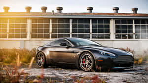 日落時分，黑色Aston Martin跑車停在舊工業建築前。