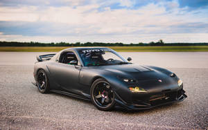 啞光黑色萬事得RX-7跑車在碎石路上，夕陽時分。