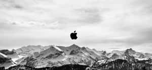 黑色Apple標誌漂浮在白雪覆蓋的山脈之上，雲層密布的天空