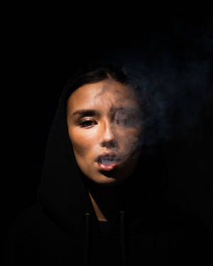 穿著黑色連帽衫的人在黑暗工作室燈光下呼出煙霧。