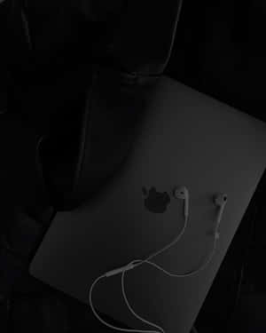 合上的手提電腦，白色耳機放在昏暗光線下的深色表面上。