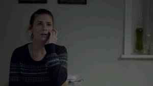 女性在昏暗房間裡打電話，背景有瓶子架，神情擔憂。 — Netflix GIF 壁紙