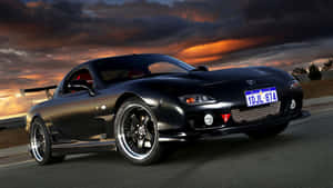 黑色Mazda RX-7跑車在日落時分行駛在道路上，天空戲劇性。