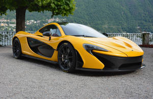 黃色McLaren P1超級跑車停在碎石路上，靠近湖泊，背景有山脈。