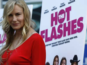 電影首映禮上身穿紅色連衣裙的女性，身後有《The Hot Flashes》海報。