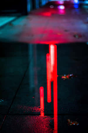 夜間城市燈光下濕漉漉的瀝青路面上的紅色發光棒