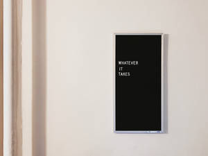 一個黑色框的勵志語錄標誌，上面寫著「WHATEVER IT TAKES」，掛在白色牆上。