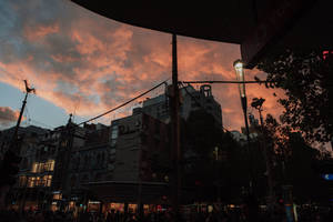 黃昏時分，繁忙城市街道上空戲劇性的橙色和粉紅色日落，建築物和雨傘形成剪影。