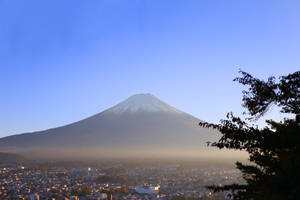 白雪覆蓋的富士山俯瞰著小鎮，前景有秋天的樹木，夕陽西下。